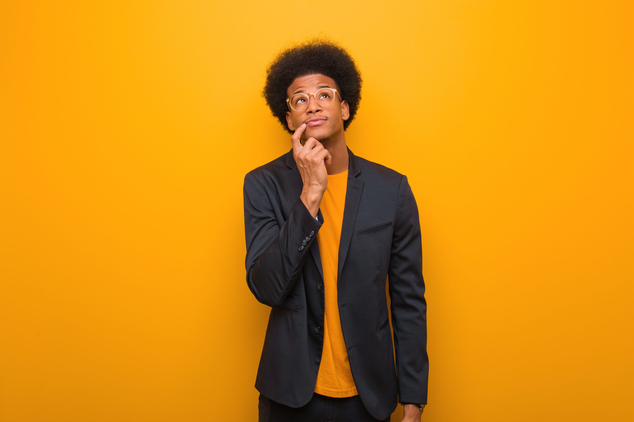 Young business african american man over an orange wall doubting and confused