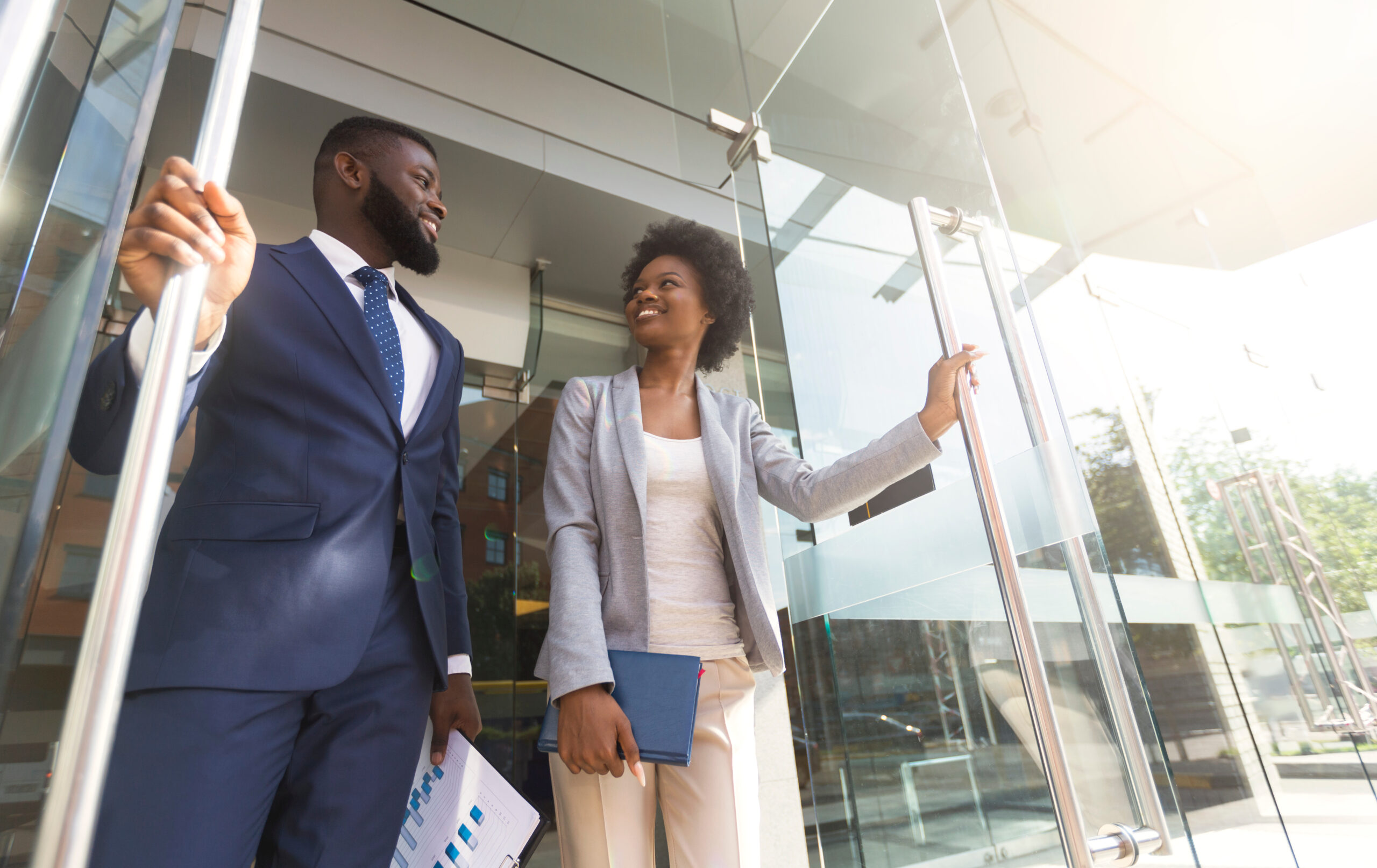 Happy confident african american business people walking out of modern office center after successful meeting. Low-Angle shot with copy space